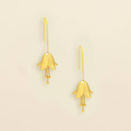 A pair of gold dangle earrings shaped like bell-shaped flowers with small bead chains hanging from the tips, shown on a plain light beige background.