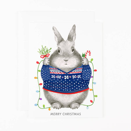 Card with illustration of a rabbit wearing a festive sweater with Christmas lights and decorations on a white background.