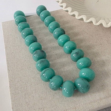 Turquoise beaded necklace on a textured surface with a white decorative object in the background