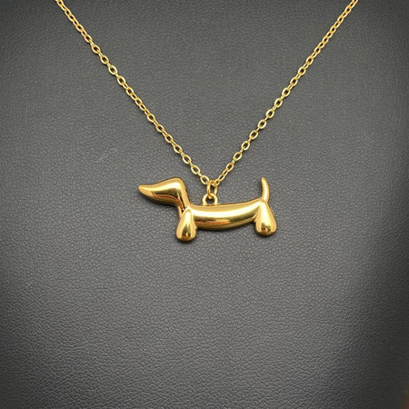 A gold dachshund-shaped pendant necklace on a matching chain, displayed against a dark textured background.