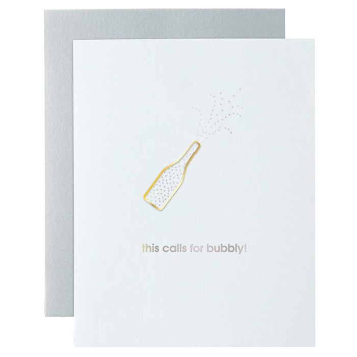 A greeting card with the phrase 'This Calls for Bubbly' printed on it, featuring a gold-colored paper clip design, presented on a background scattered with confetti.