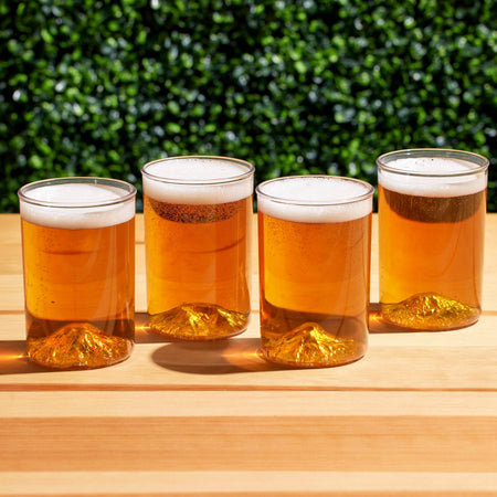 Four glasses of beer on a wooden surface with a green bush background