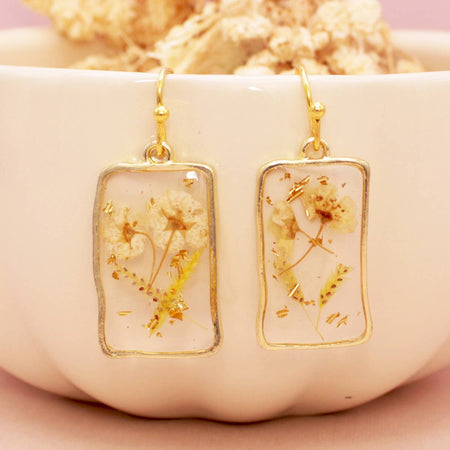 Gold-framed earrings with dried flowers on a beige dish