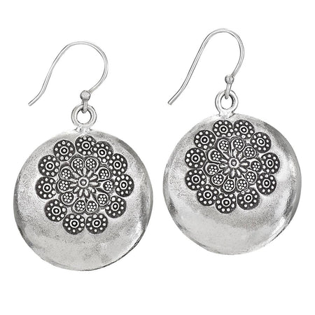 A pair of silver-toned round drop earrings with a textured finish and an intricate floral mandala pattern on the front, hanging from fishhook wires against a plain white background.