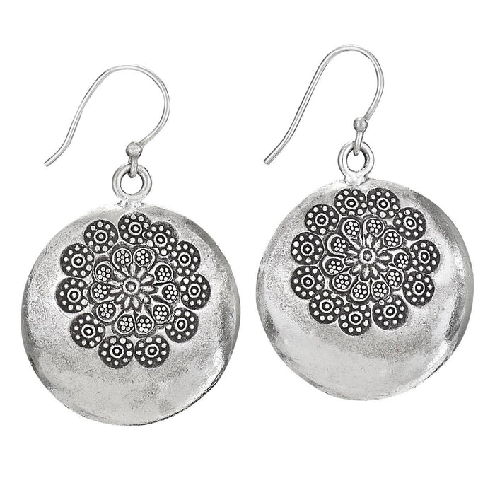 A pair of silver-toned round drop earrings with a textured finish and an intricate floral mandala pattern on the front, hanging from fishhook wires against a plain white background.