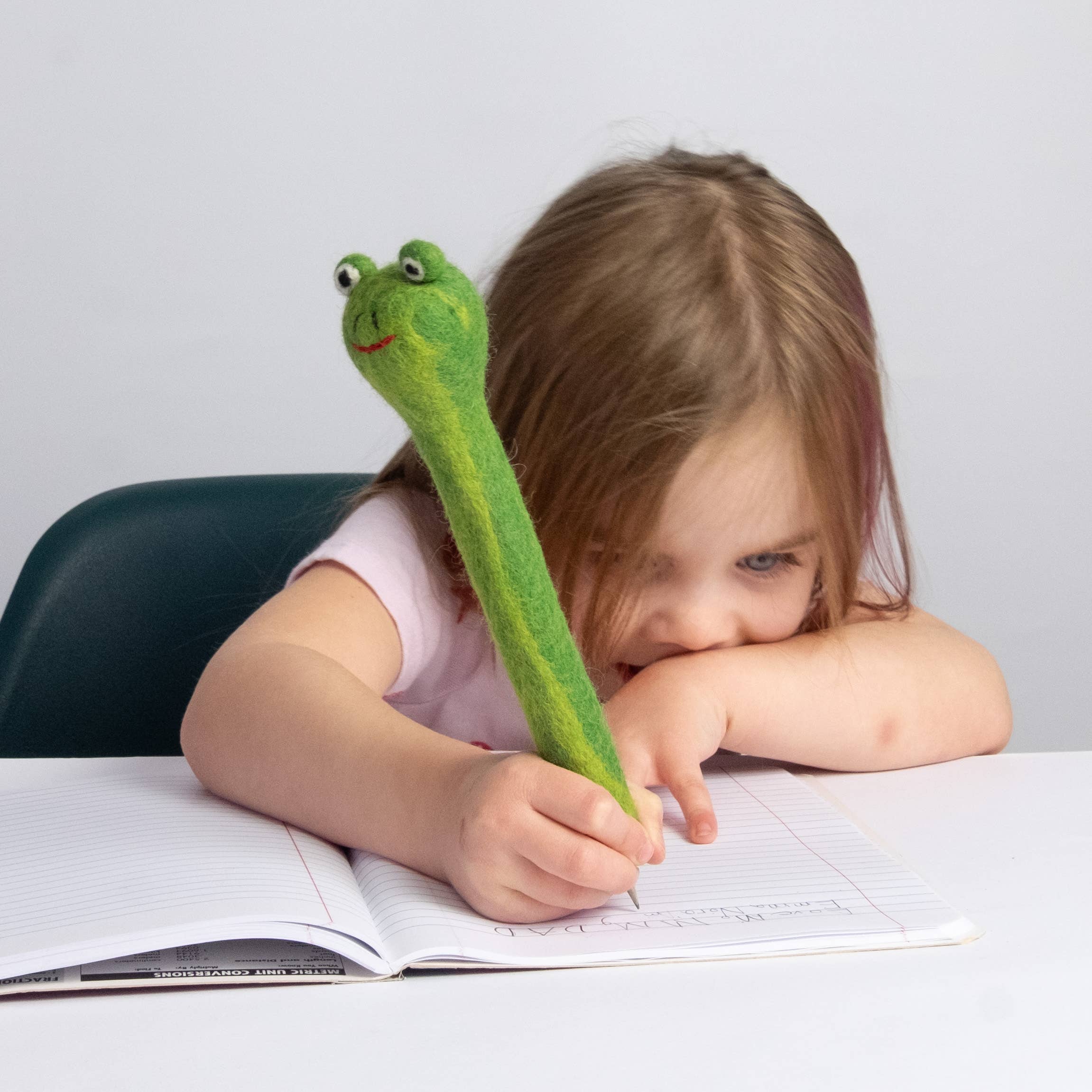 Child with a green frog-shaped pencil topper on a white background