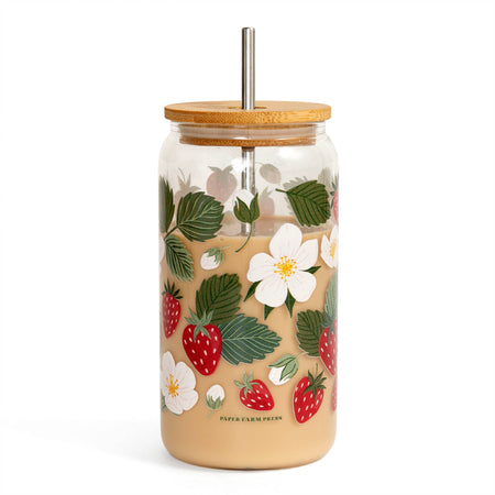 Glass tumbler with floral and strawberry design, wooden lid, and metal straw on a white background.