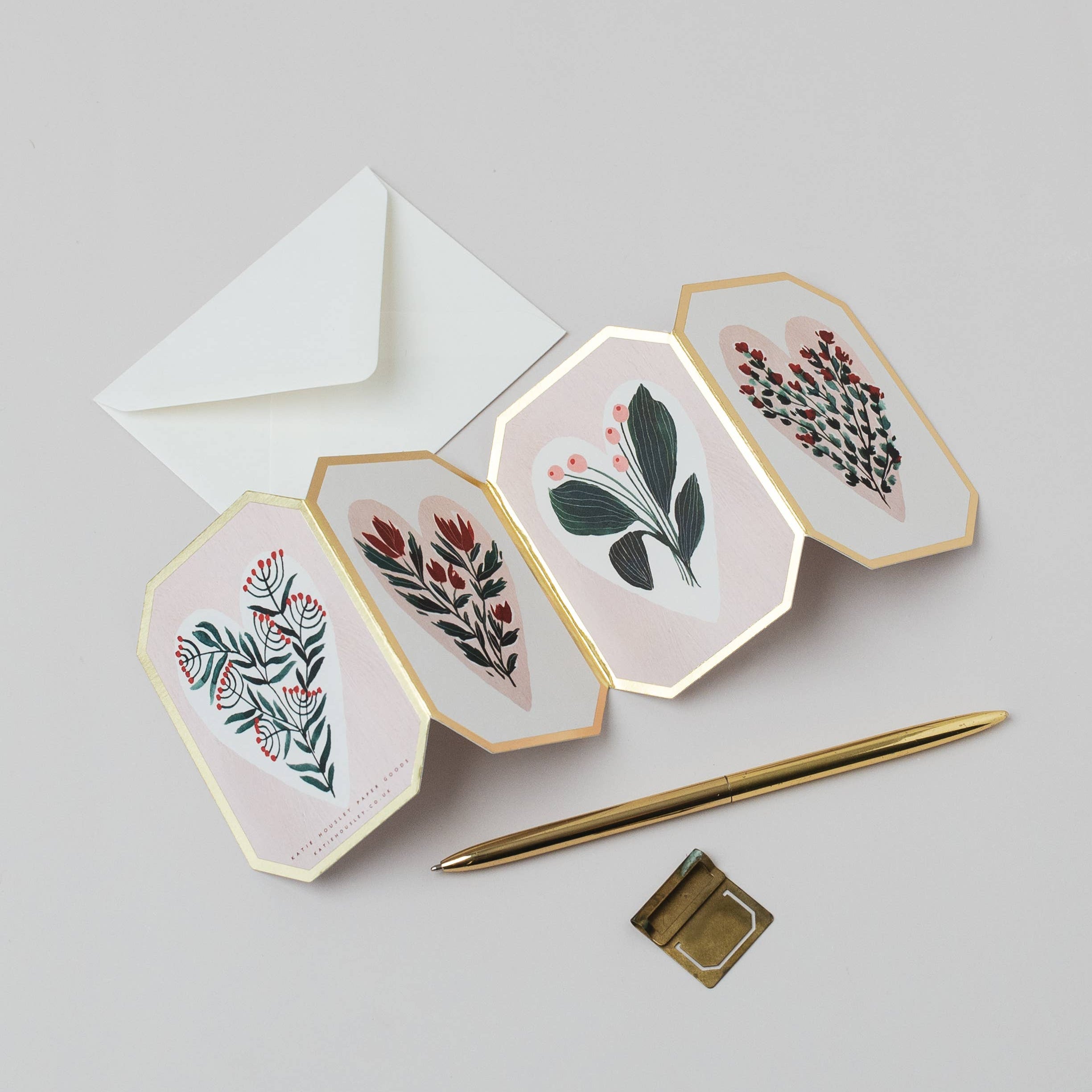 Four hexagonal cards with floral designs, a white envelope, and a gold pen on a light gray background.