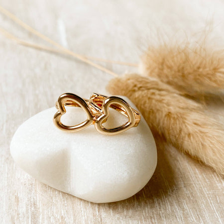 Gold heart-shaped huggie earrings on a white stone with dried plant elements