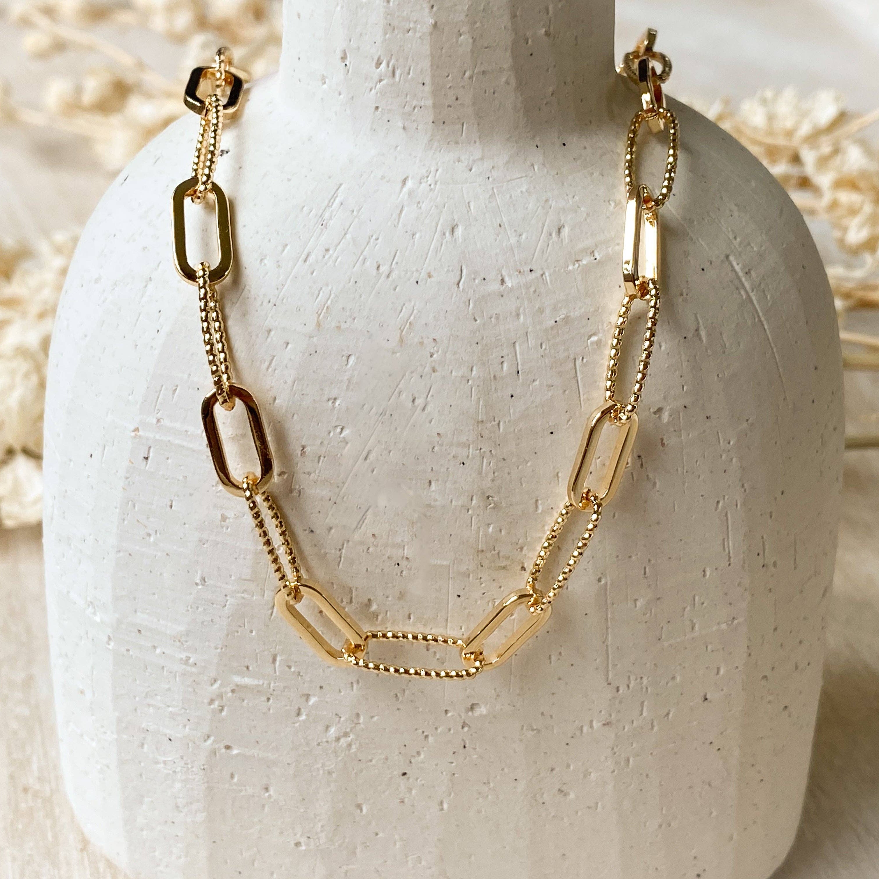 Gold chain necklace on a white ceramic stand with a neutral background