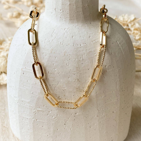 Gold chain necklace on a white ceramic stand with a neutral background