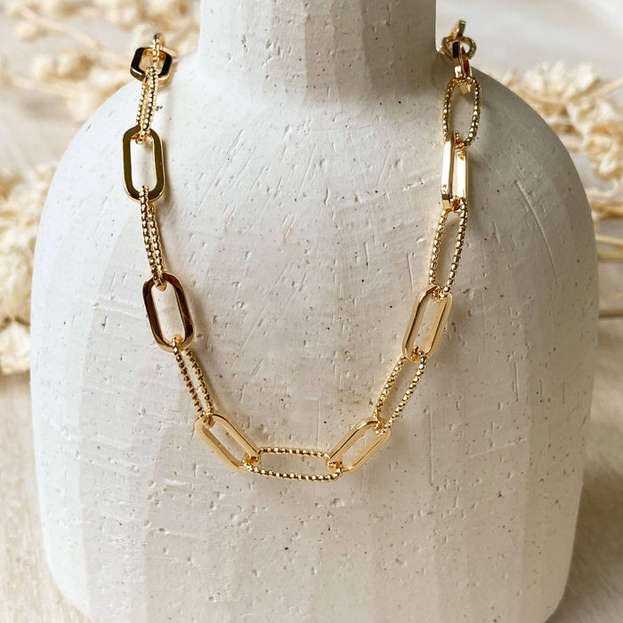 Gold chain necklace on a white ceramic stand with a neutral background