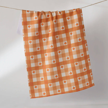 An orange and white gingham kitchen towel with small pumpkin prints, hanging from a string against a light gray background.