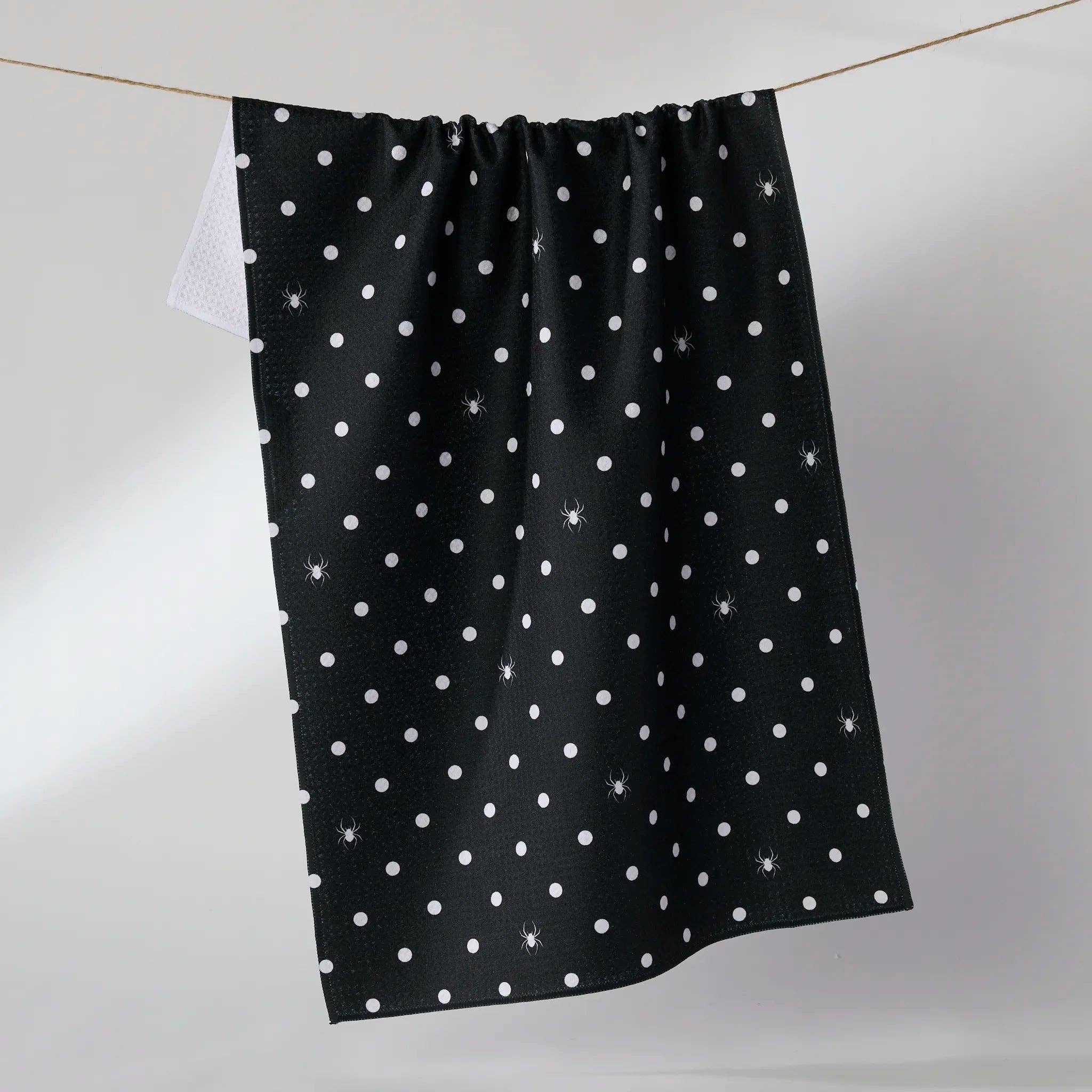 Black towel with white polka dots and spiders hanging on a line against a light gray background
