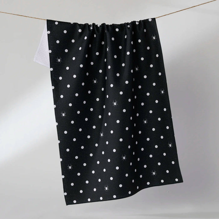 Black towel with white polka dots and spiders hanging on a line against a light gray background