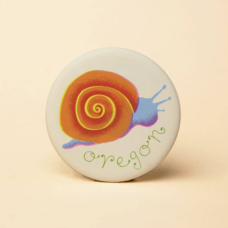 Round button with a colorful snail design and 'Oregon' text on a beige background