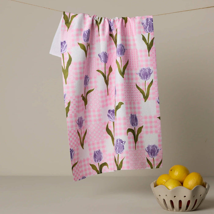 Towel with tulip pattern on a pink checkered background hanging on a line, with a bowl of lemons below.