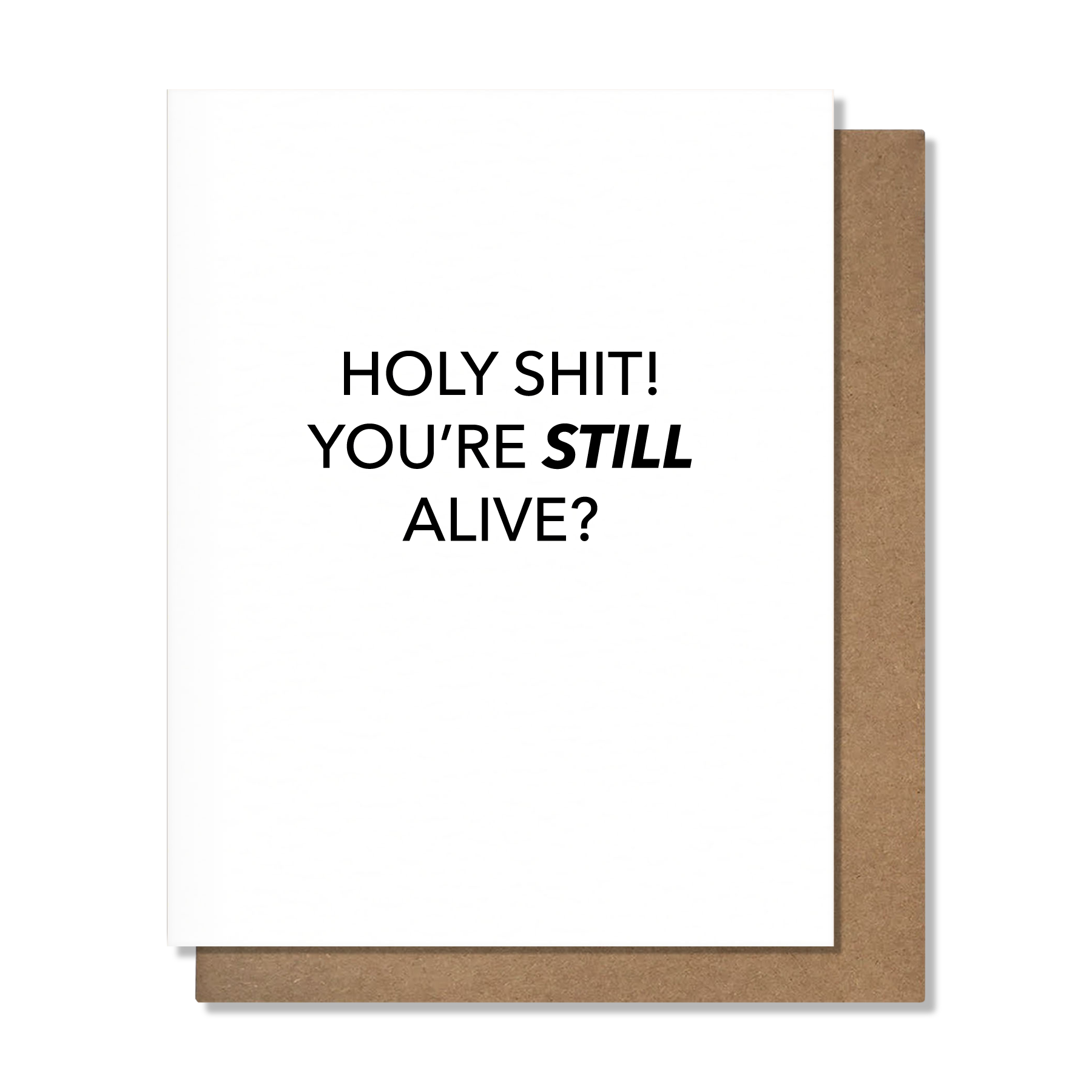 A white greeting card with bold black text reading 'HOLY SHIT! YOU'RE STILL ALIVE?' and a brown kraft envelope behind it, shown on a clean white background.