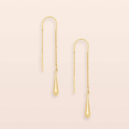 A pair of gold dangle earrings with textured chain links and teardrop-shaped drop pendants, displayed against a solid pale pink background.