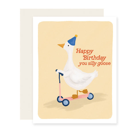 A birthday greeting card featuring an illustration of a white goose riding a pink scooter and wearing a blue party hat, with the text 'Happy Birthday you silly goose' in red. The card is shown with a light beige envelope behind it on a white background.