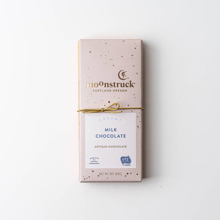 A Moonstruck Portland Oregon Milk Chocolate artisan chocolate bar in its original packaging, tied with a thin gold string, on a clean white background.
