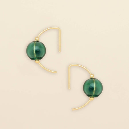 A pair of gold hoop earrings with a translucent green glass bead at the center, displayed on a light beige background.