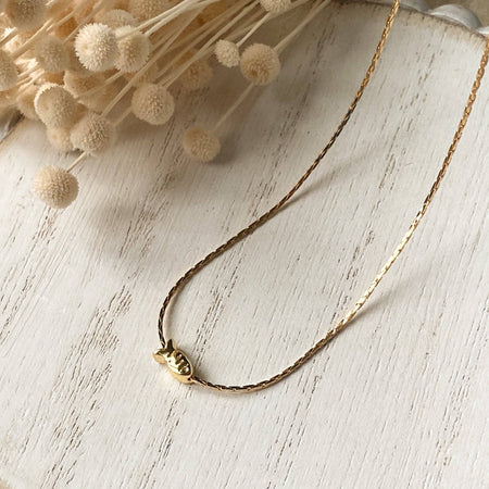 Gold fish necklace on a round wooden surface with dried flowers