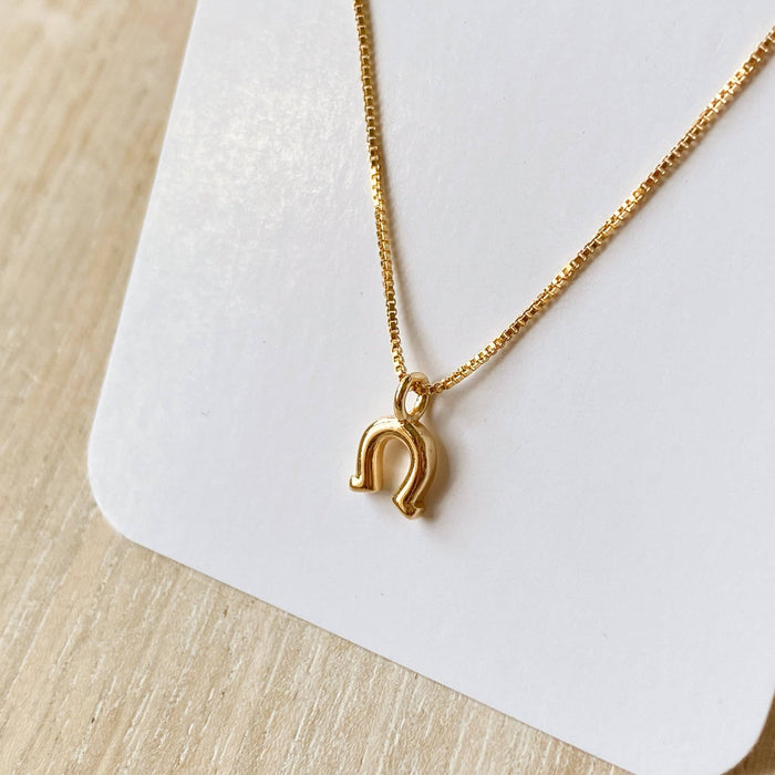Gold necklace with a horseshoe pendant on a white card