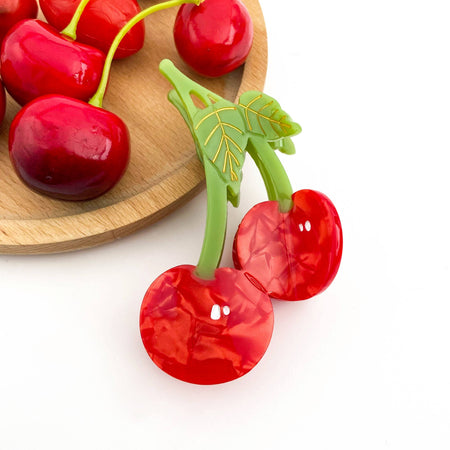 Red cherry-shaped hair clip with green stems on a white background