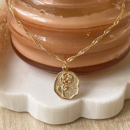 Gold necklace with a rose pendant on a decorative stand.