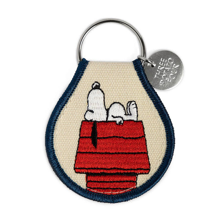 Keychain with Snoopy on a doghouse design, featuring a brand logo.