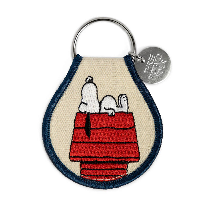 Keychain with Snoopy on a doghouse design, featuring a brand logo.