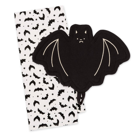 A black bat-shaped potholder with cream-colored stitched wing details, shown next to a white fabric napkin or tea towel printed with a black bat, moon, and star pattern, on a solid white background.