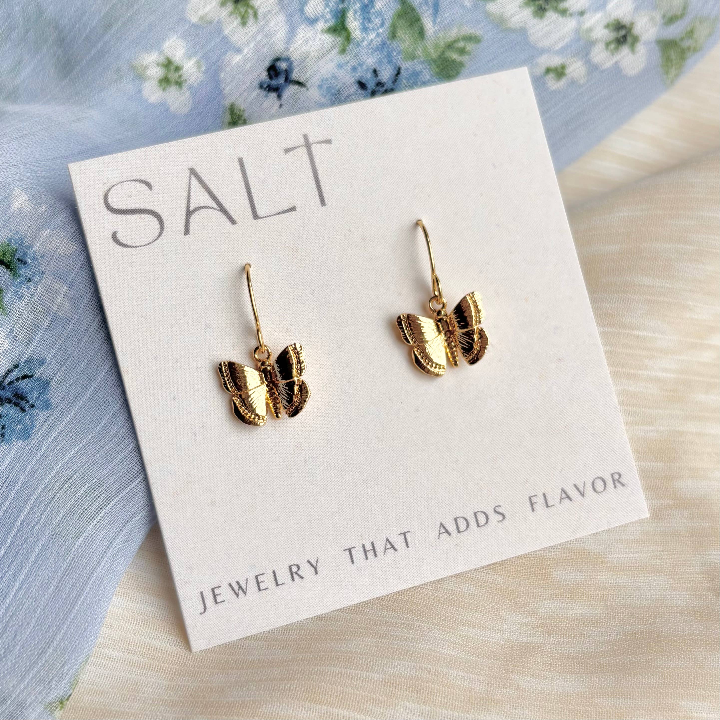 Gold butterfly earrings on a 'SALT' branded card with floral background