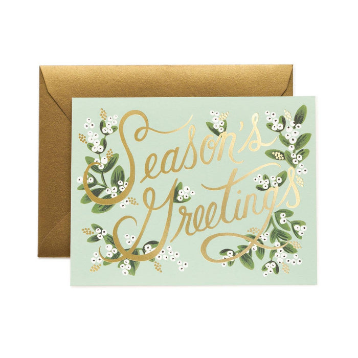 Greeting card with 'Season's Greetings' text and gold foil design on a light green background, accompanied by a brown envelope.