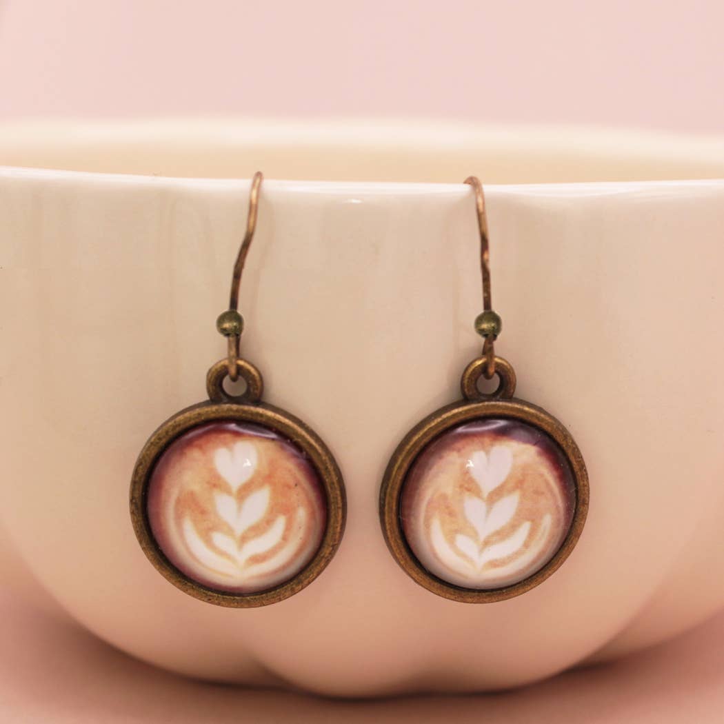 Earrings with latte art design in bronze frames on a pink background