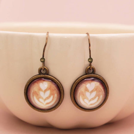 Earrings with latte art design in bronze frames on a pink background