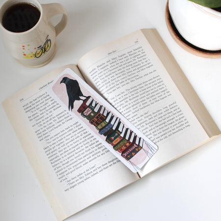Open book with a bookmark featuring a bird and piano keys, next to a mug on a white surface.