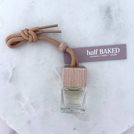 Small bottle with wooden cap and tassel on a marble surface, branded 'half BAKED'.