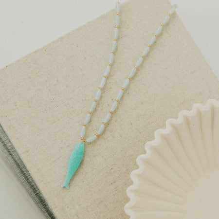 Necklace with a turquoise fish pendant on a textured surface