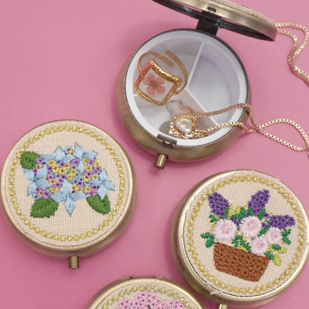 Three round embroidered mini organizer cases with floral designs on a pink background.