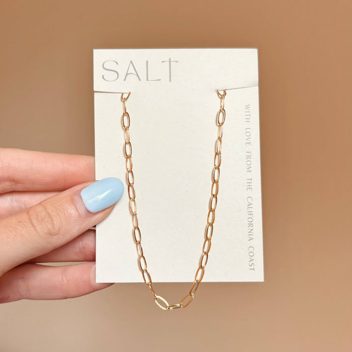 Gold chain necklace on a 'SALT' branded card held by a hand with light blue nail polish.