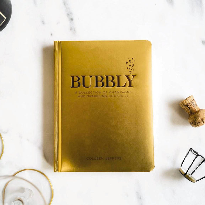Gold book titled 'Bubbly' on a marble surface with champagne bottle and glasses.