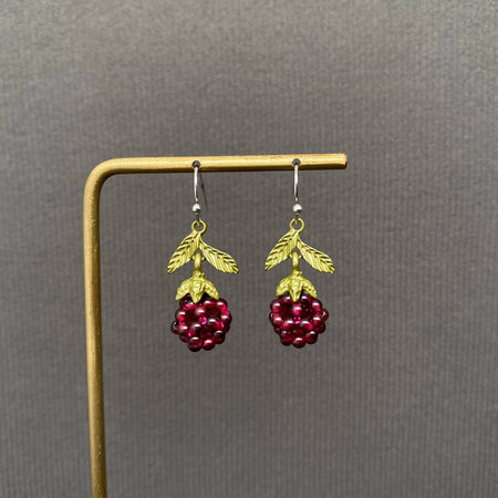Pair of earrings with red berry-like charms on a gold stand against a gray background