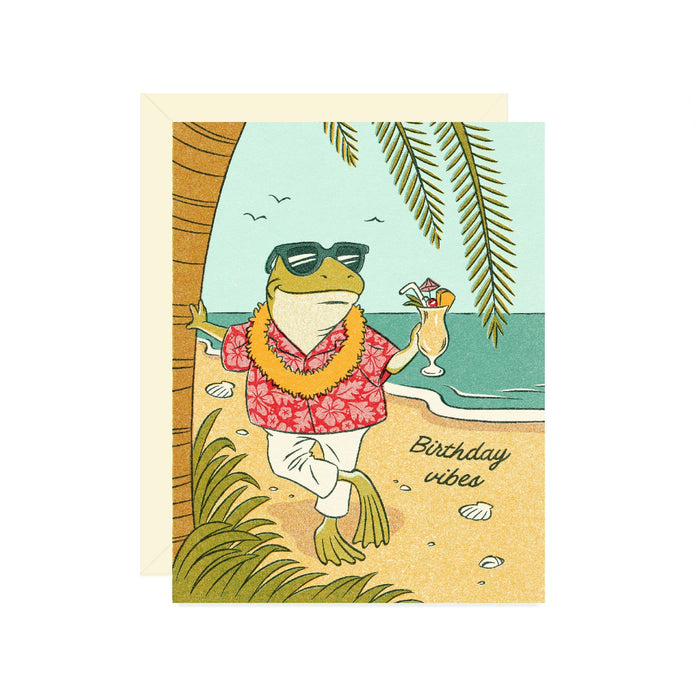 A tropical beach-themed birthday card featuring an anthropomorphic frog wearing sunglasses, a red floral shirt, and a yellow lei while holding a cocktail. The card reads 'Birthday vibes' and is shown with its cream envelope against a plain white background.