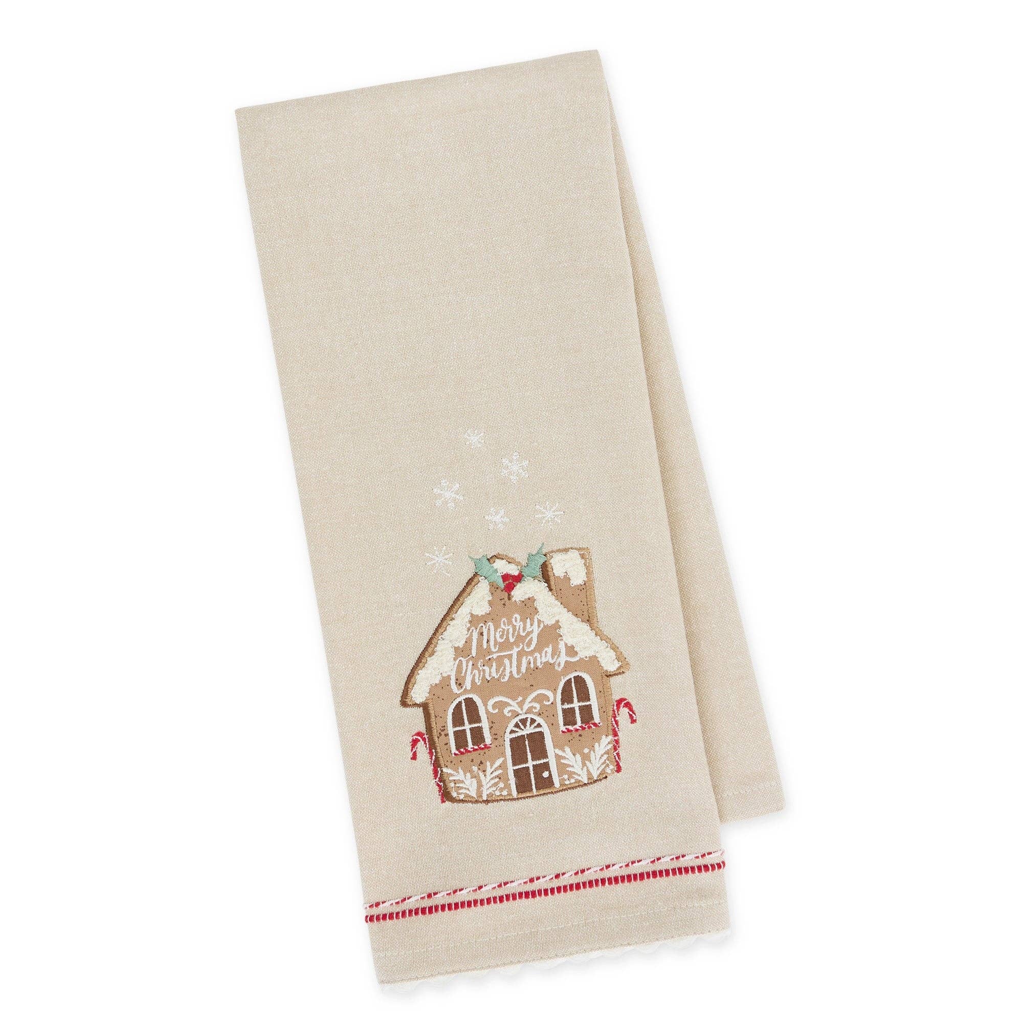 A beige kitchen towel with a festive embroidered gingerbread house design that reads 'Merry Christmas' and small snowflake motifs, shown on a clean white background.
