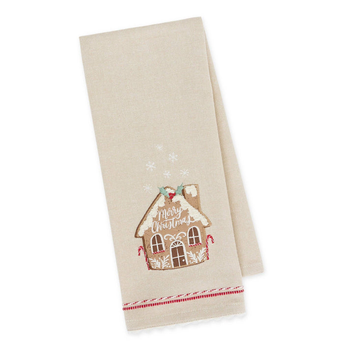 A beige kitchen towel with a festive embroidered gingerbread house design that reads 'Merry Christmas' and small snowflake motifs, shown on a clean white background.