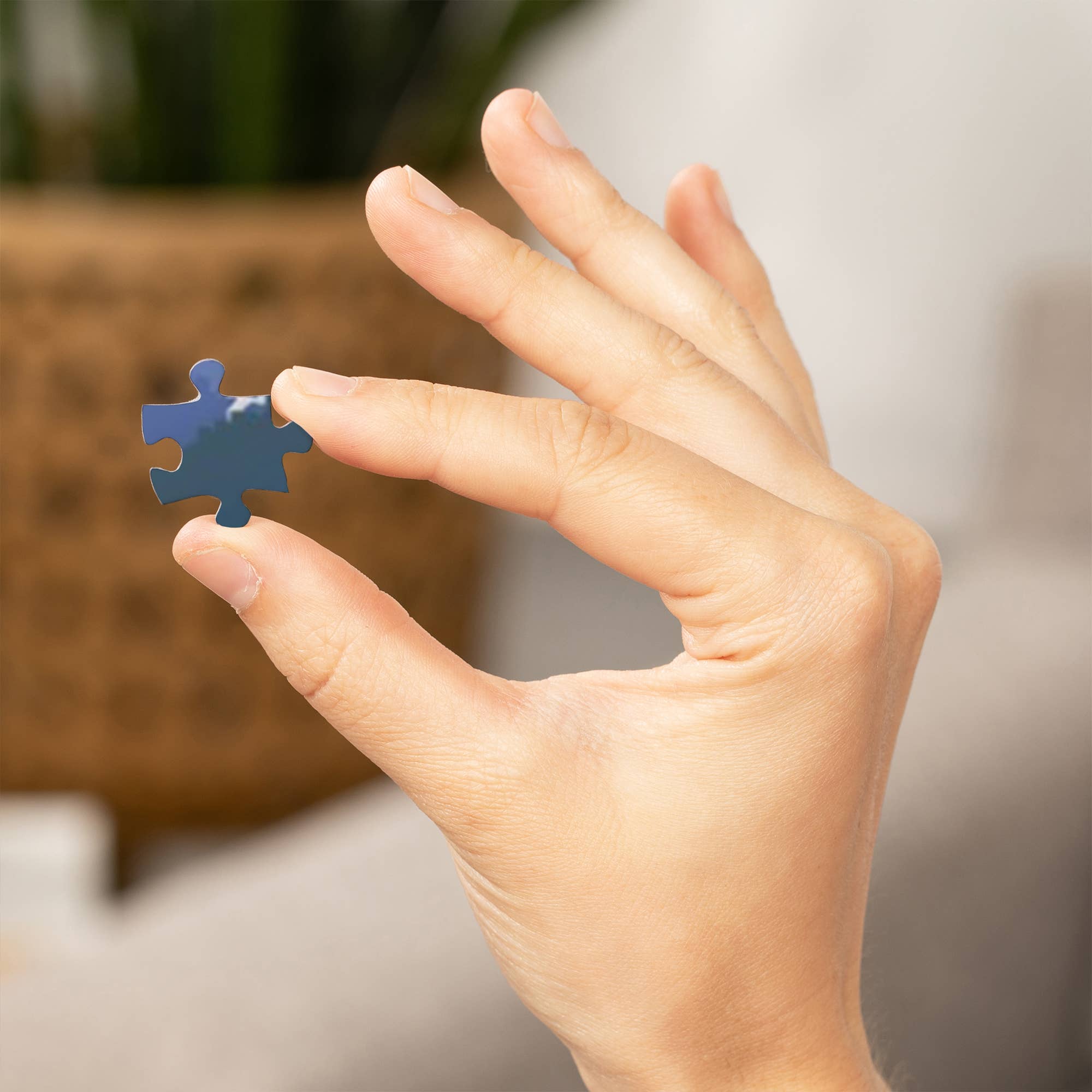 Hand holding a blue puzzle piece against a blurred indoor background