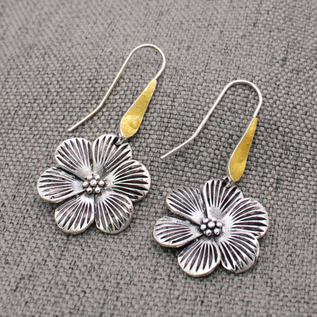 Floral silver earrings with gold accents on a textured gray surface