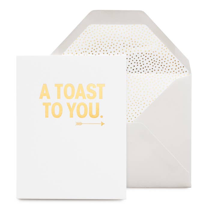 white card that reads " a toast to you" in gold foil with an arrow illustration